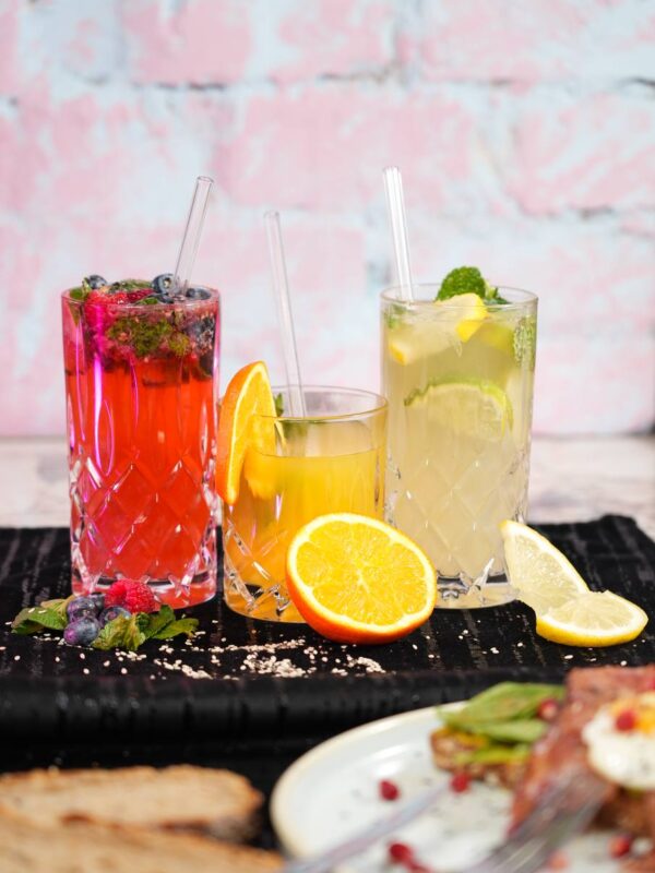 Drei erfrischende Getränke: Rote Beeren-Limonade, Orangensaft und Minzlimonade, serviert in Kristallgläsern